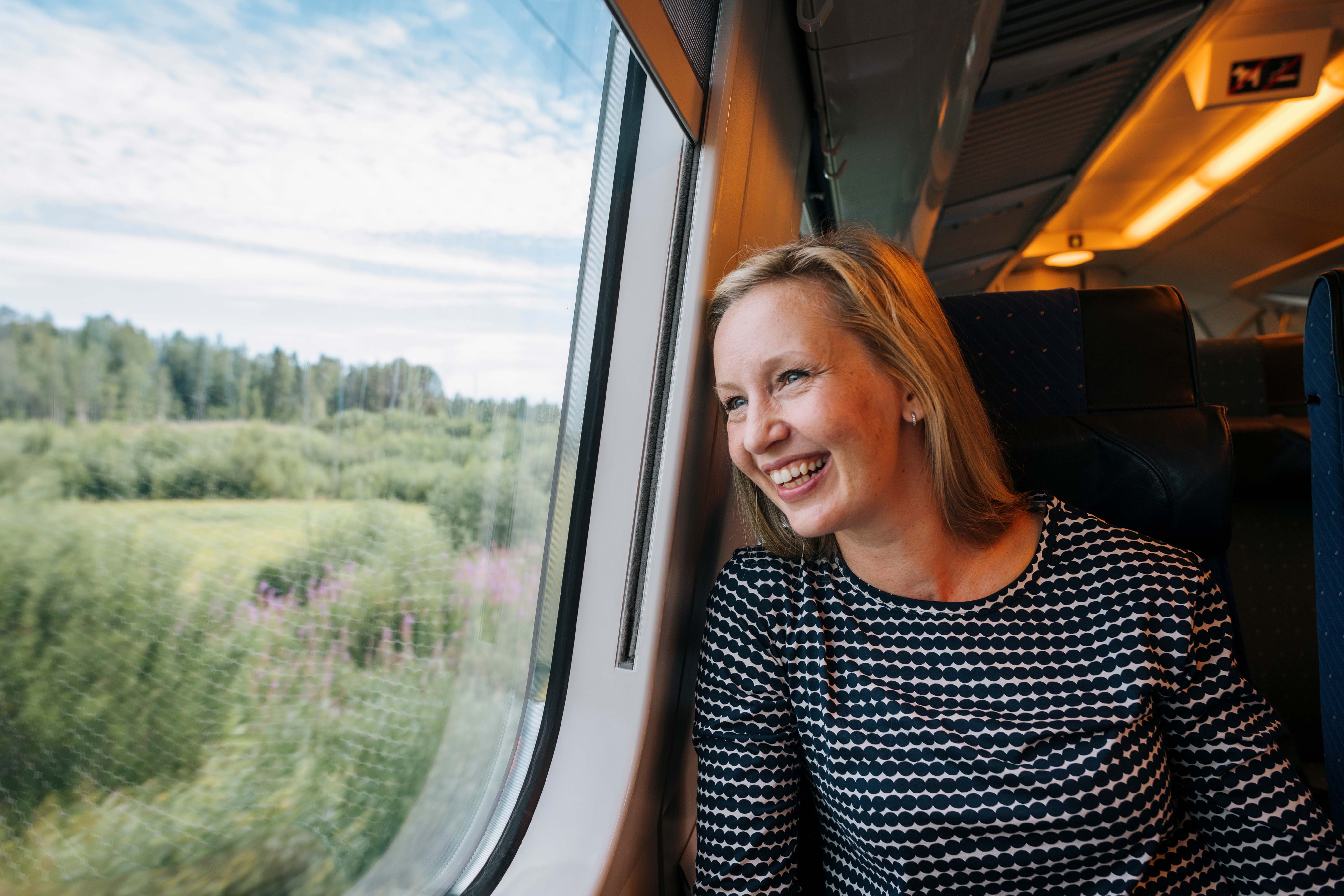 Une femme voyageant en train en Finlande est en train de regarder les paysages qui défilent.