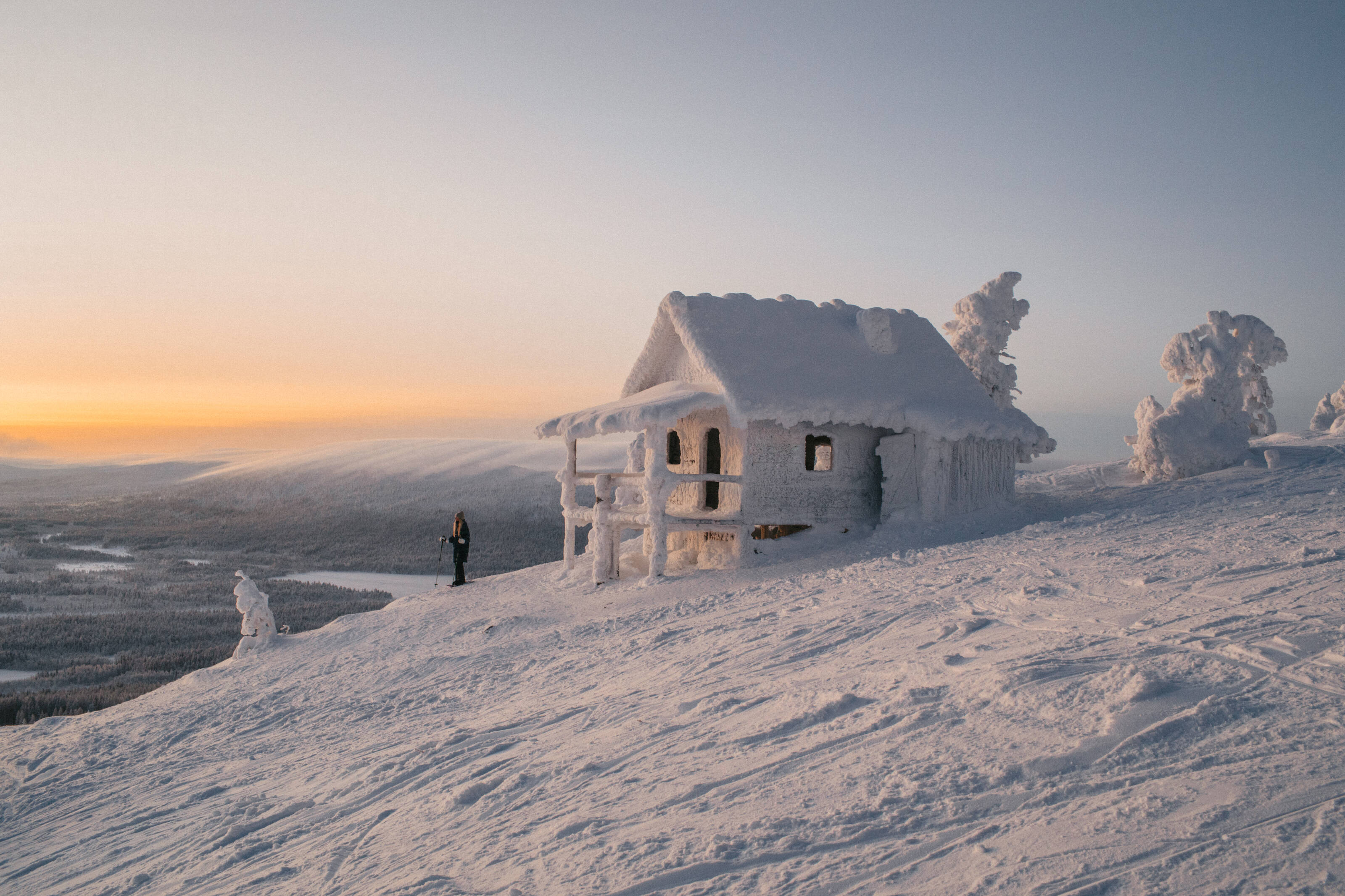 Una raqueta de nieve junto a una cabaña totalmente cubierta de hielo y nieve en la cima de una colina.